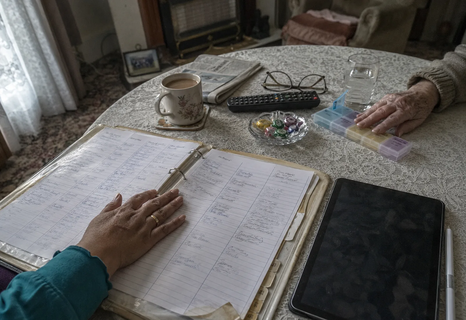 A handwritten paper care plan folder open beside a switched-off tablet on a client's dining table.