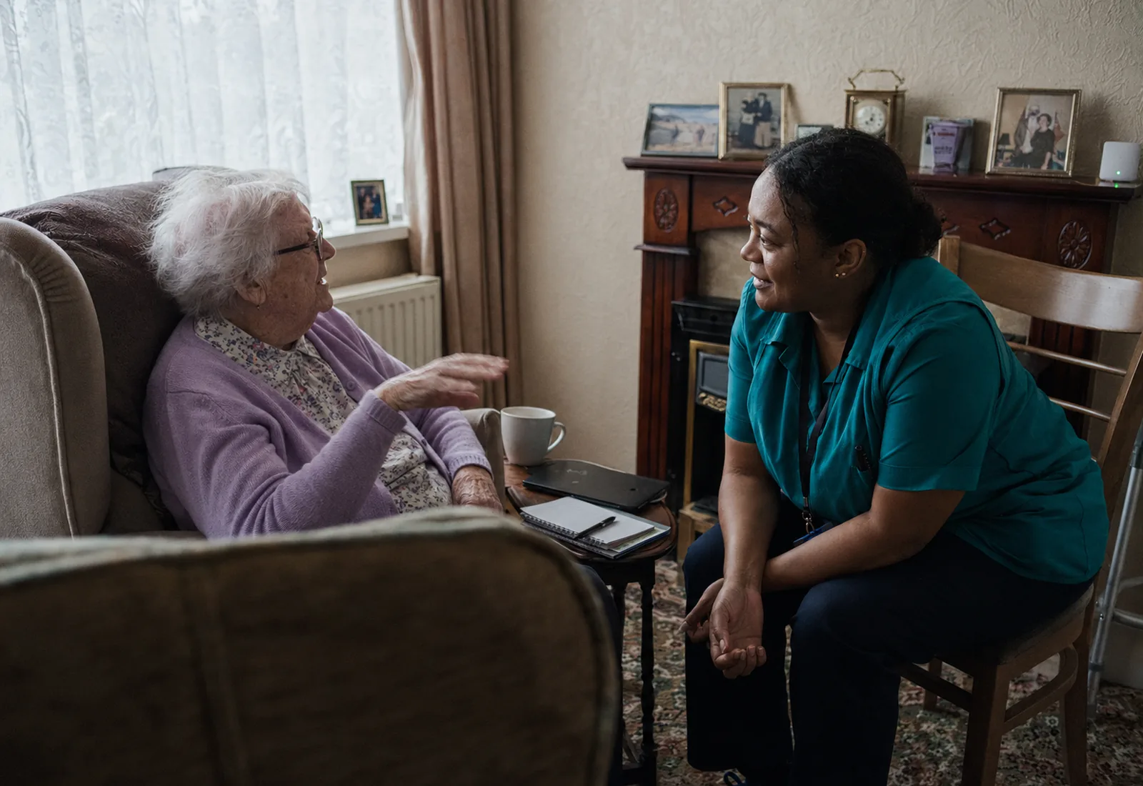 A care worker sitting with an older client in her front room, listening as she talks.
